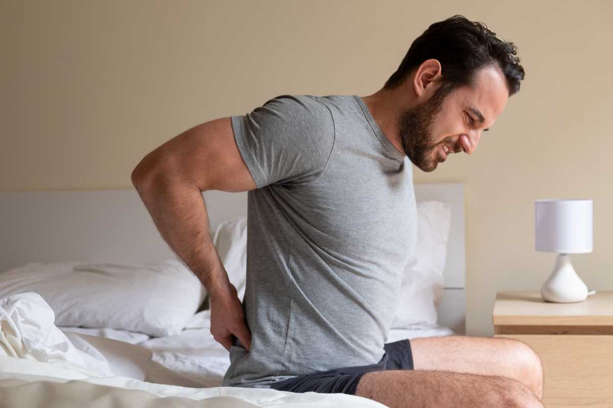 Man sitting in bed holding his back