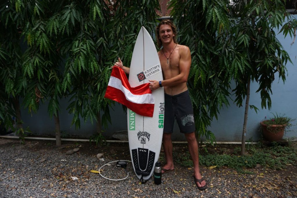 Manuel Paulitsch bei der Surf-WM 2023 mit Österreichfahne und Surfbrett
