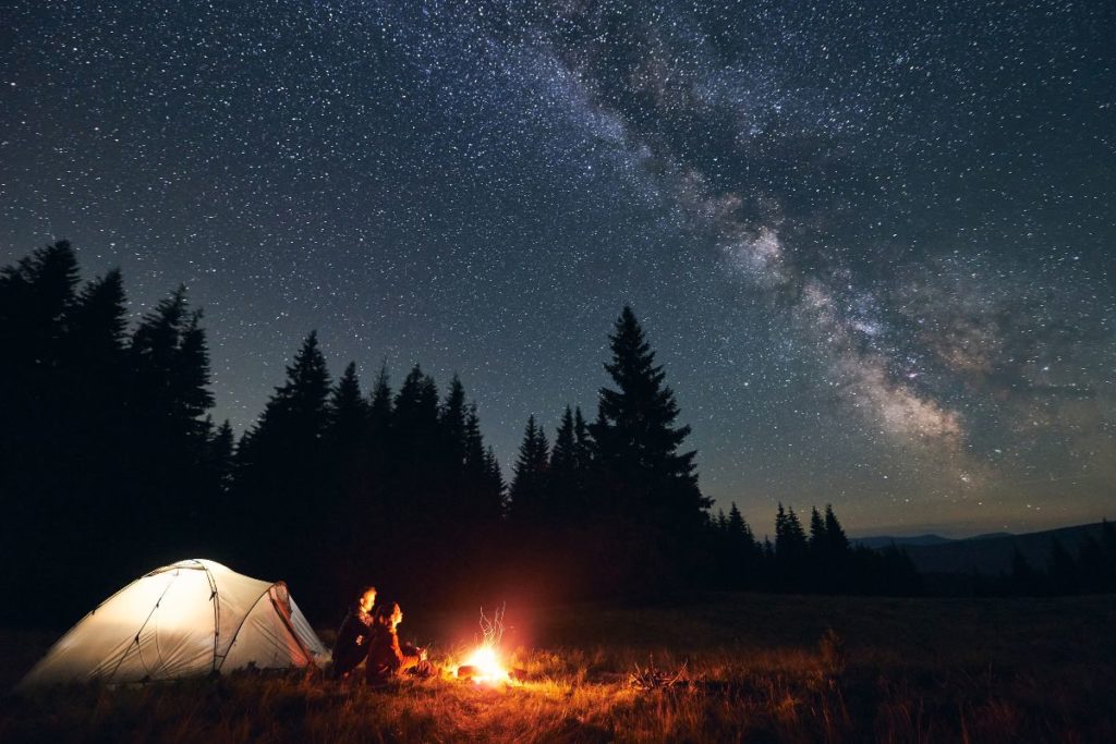 Zelt mit Lagerfeuer unter Sternenhimmel im Wald